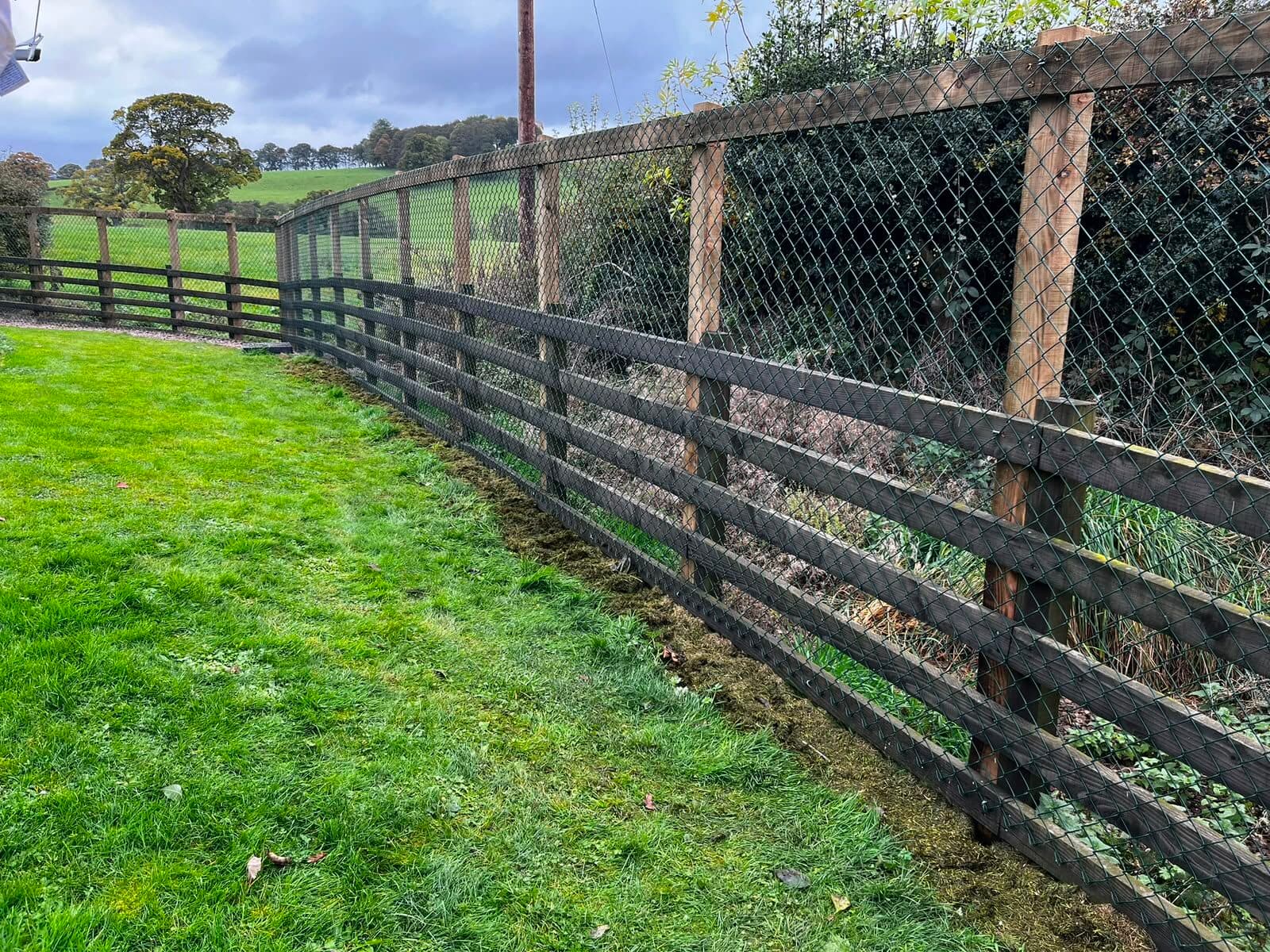 Post-and-rail fencing with wire mesh along a field boundary